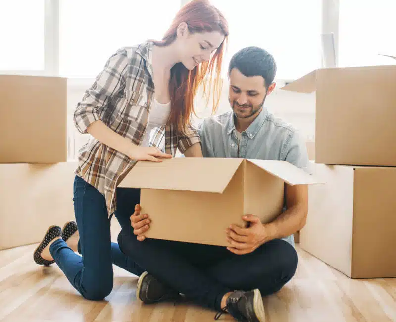 Couple unpacking furniture moving company boxes together indoors.